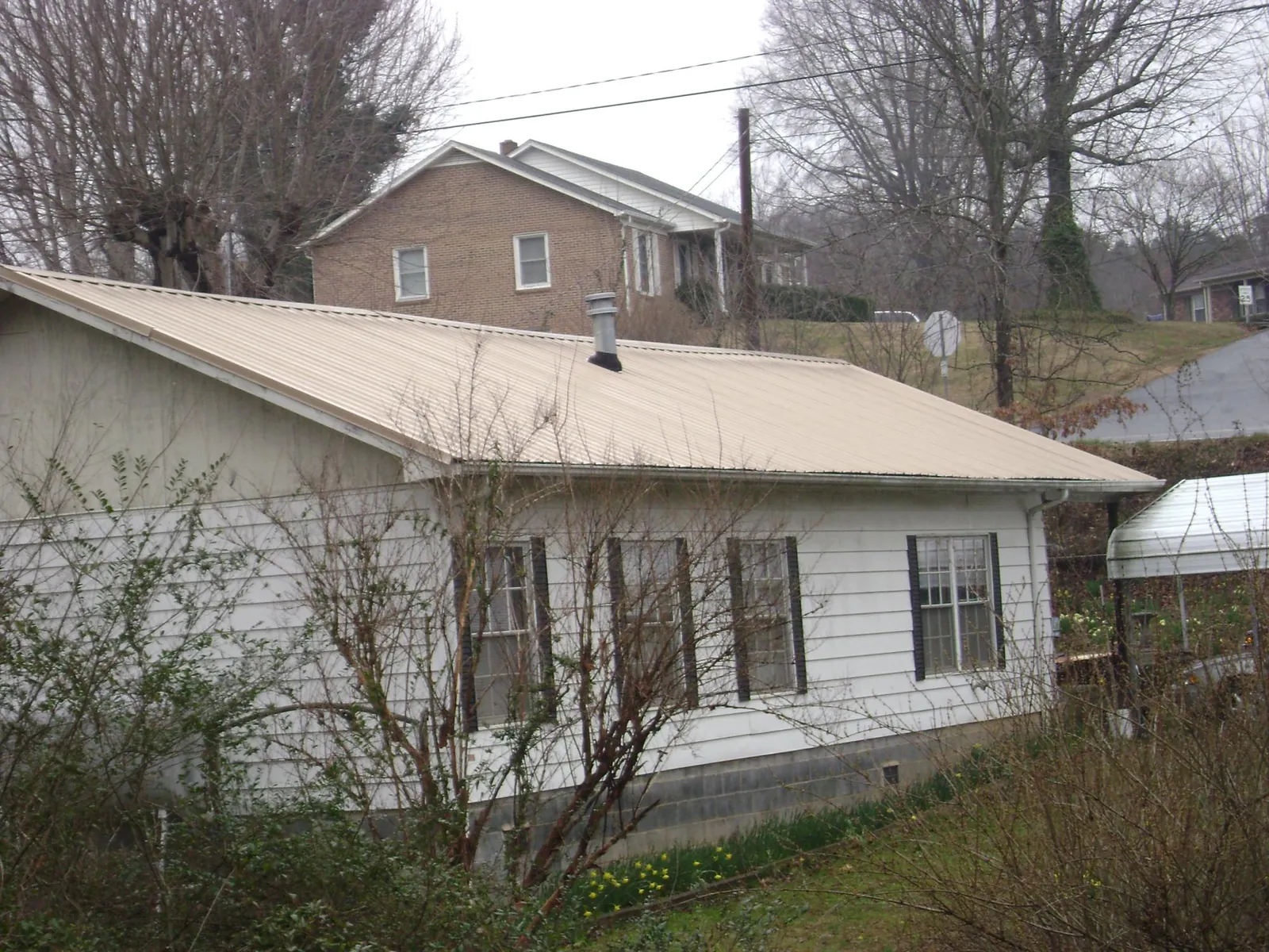 Tan metal roof on a white sided house set into a hillside — Commercial Roofing by Roofing Brothers in Utica